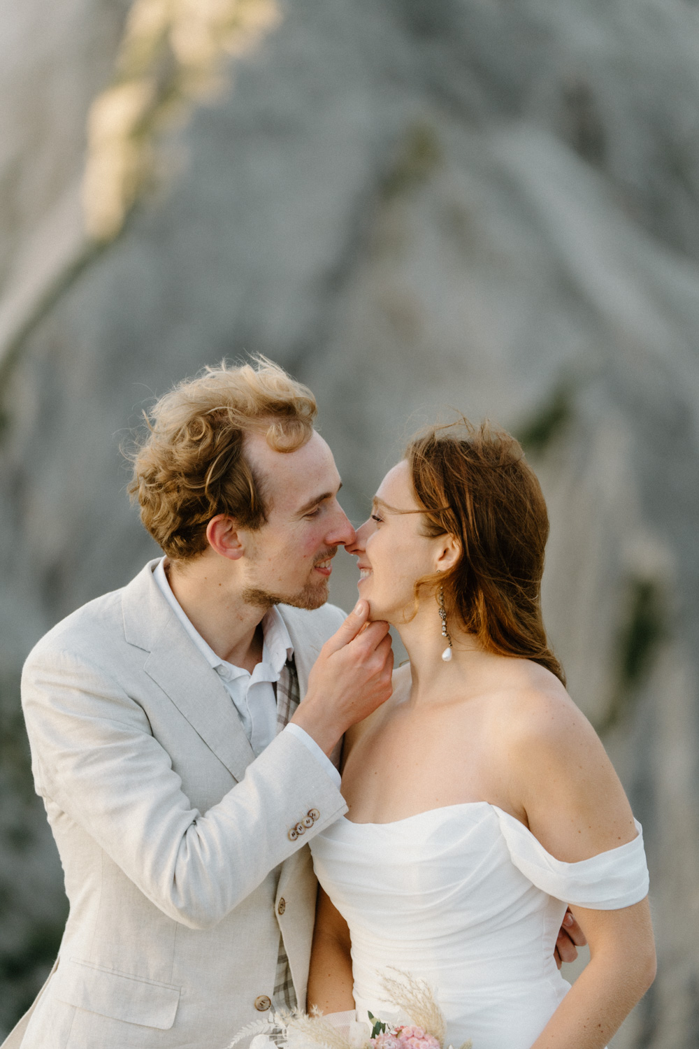 A couple in wedding attire snuggles close and kisses with Cadini di Misurina mountain behind them during their Italian Dolomites elopement. 