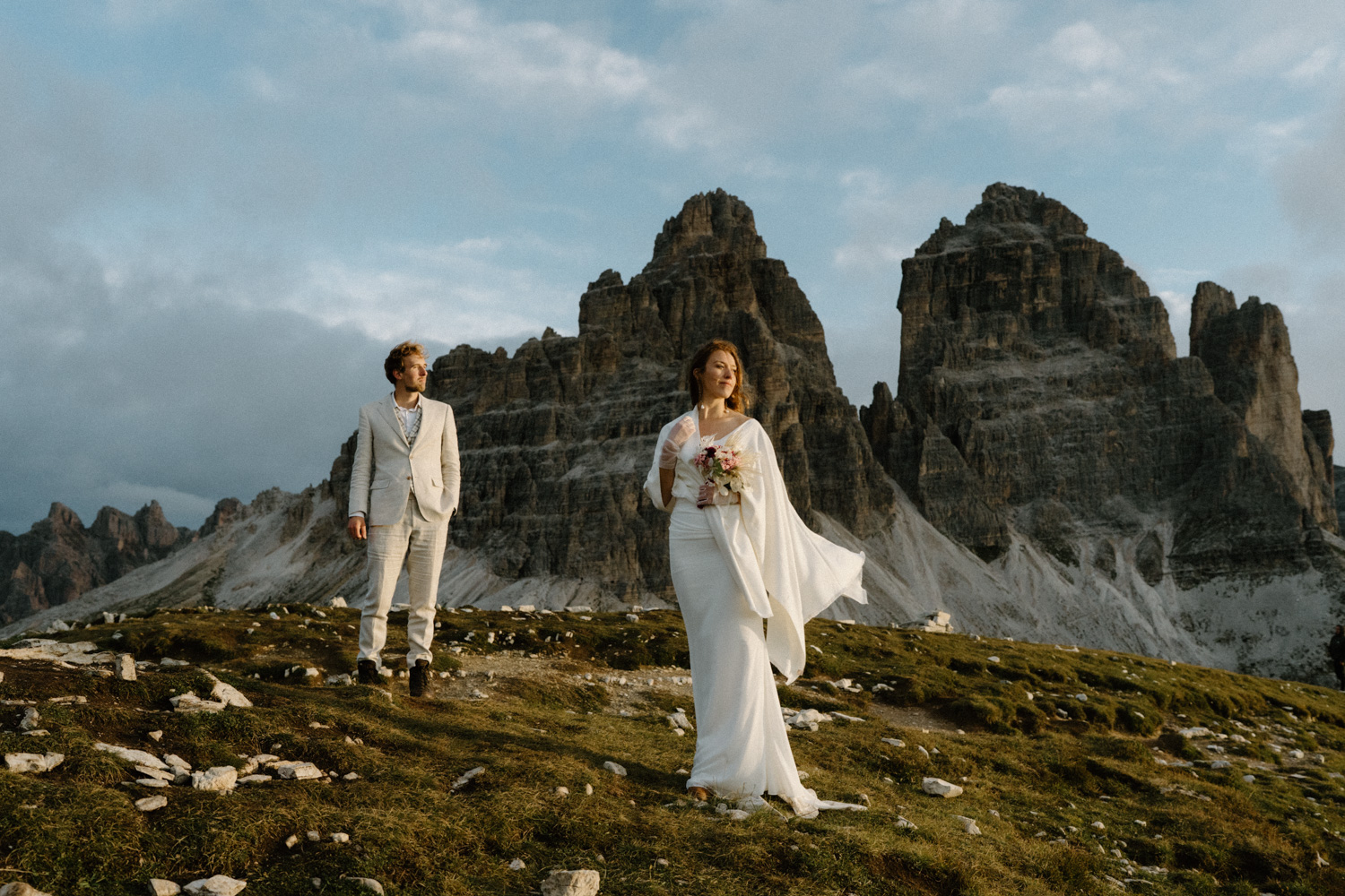 A couple in wedding attire stand in front of the Tre Cime as they watch the sun rise over the hills during their Italian Dolomites elopement