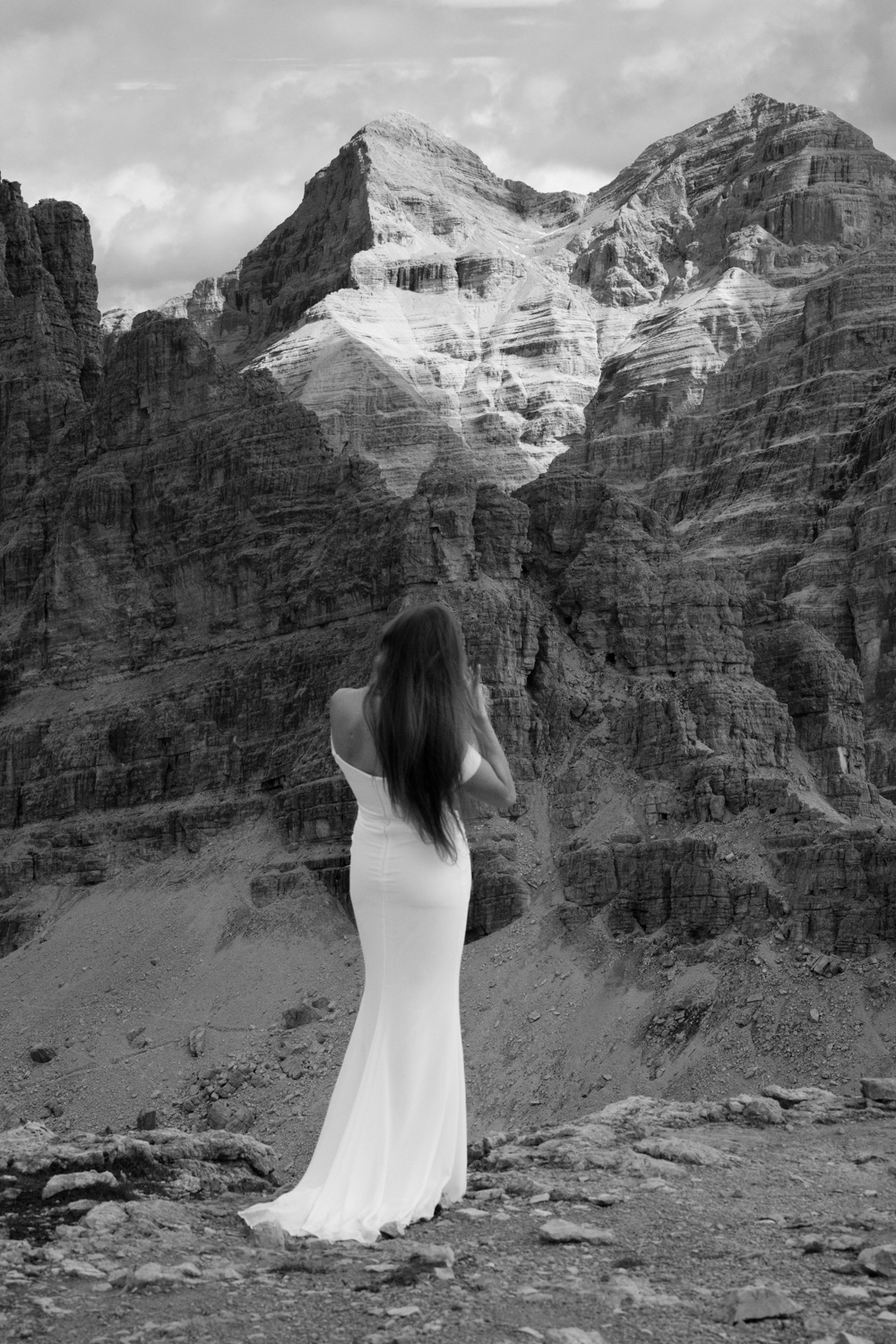 A black and white photo of a bride standing in front of a mountain range towering above her during her Italian Dolomites elopement. 