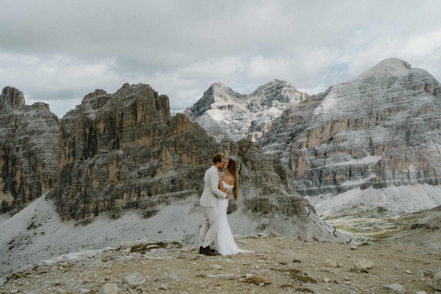 A couple embraces and kisses in front of an orange mountain range during their Italian Dolomites elopement. 