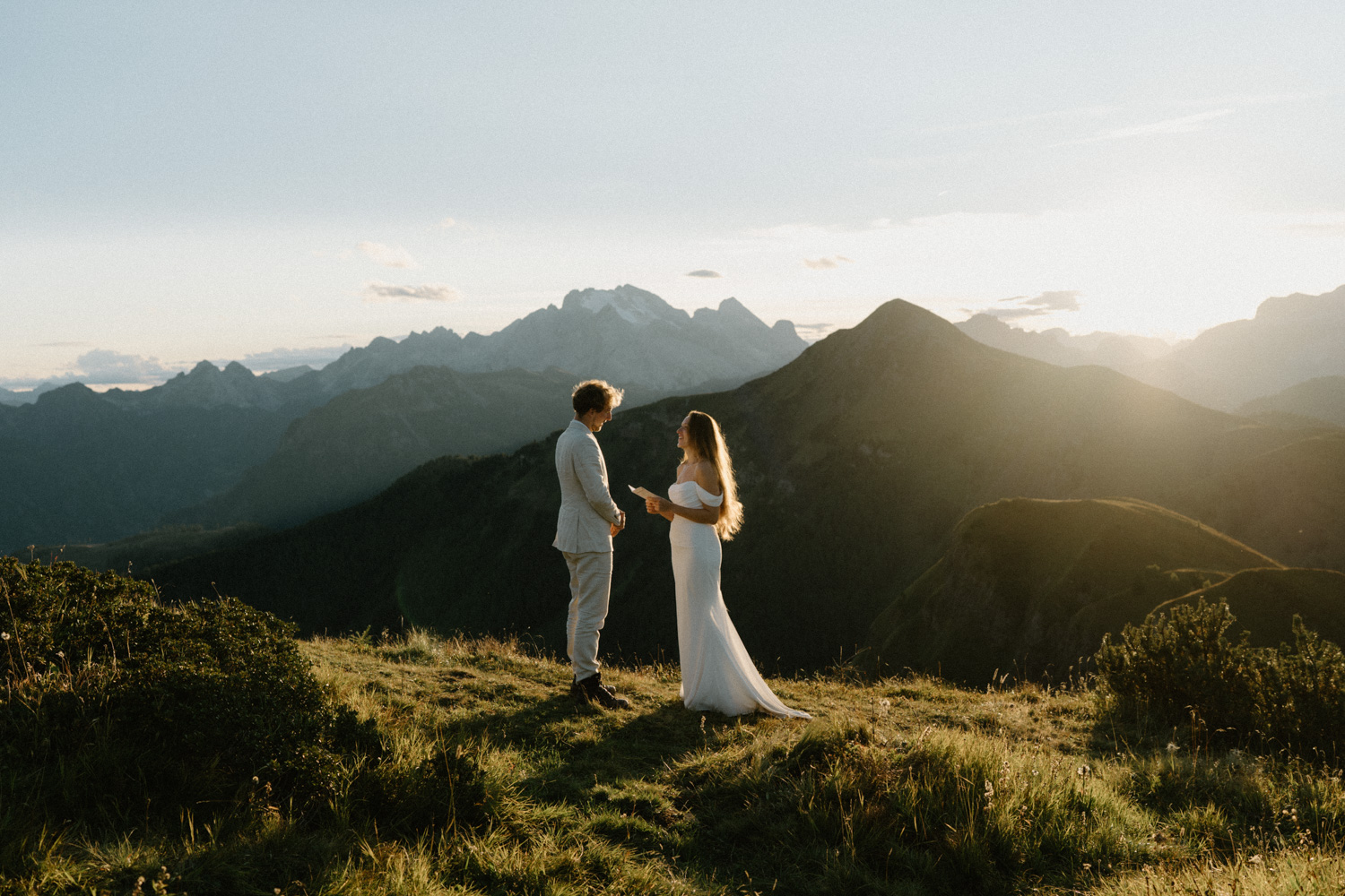 A couple in wedding attire stand and exchange vows with the mountains behind them as the sun sets during their Italian Dolomites elopement. 