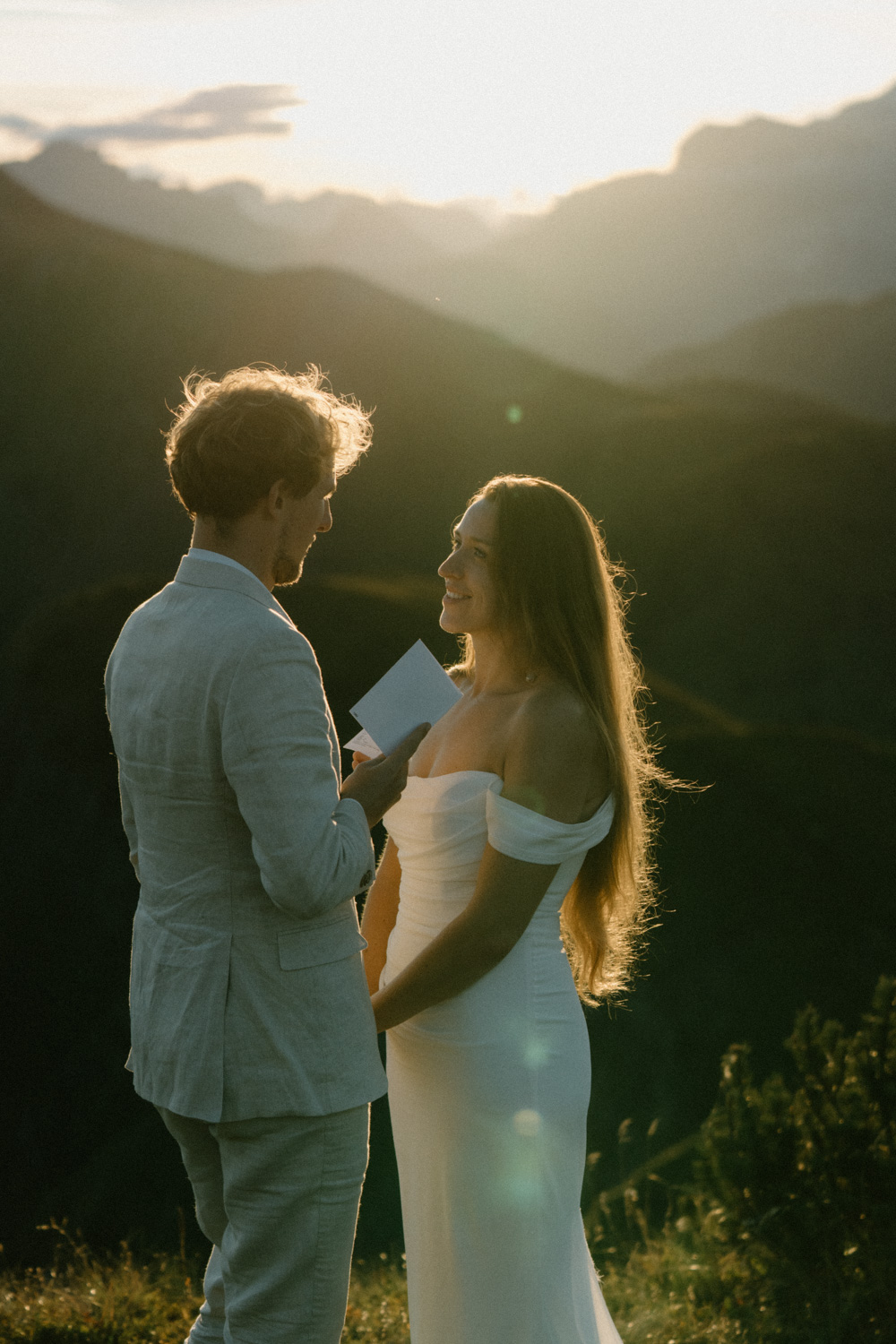 A couple in wedding attire stand and exchange vows with the mountains behind them as the sun sets during their Italian Dolomites elopement. 
