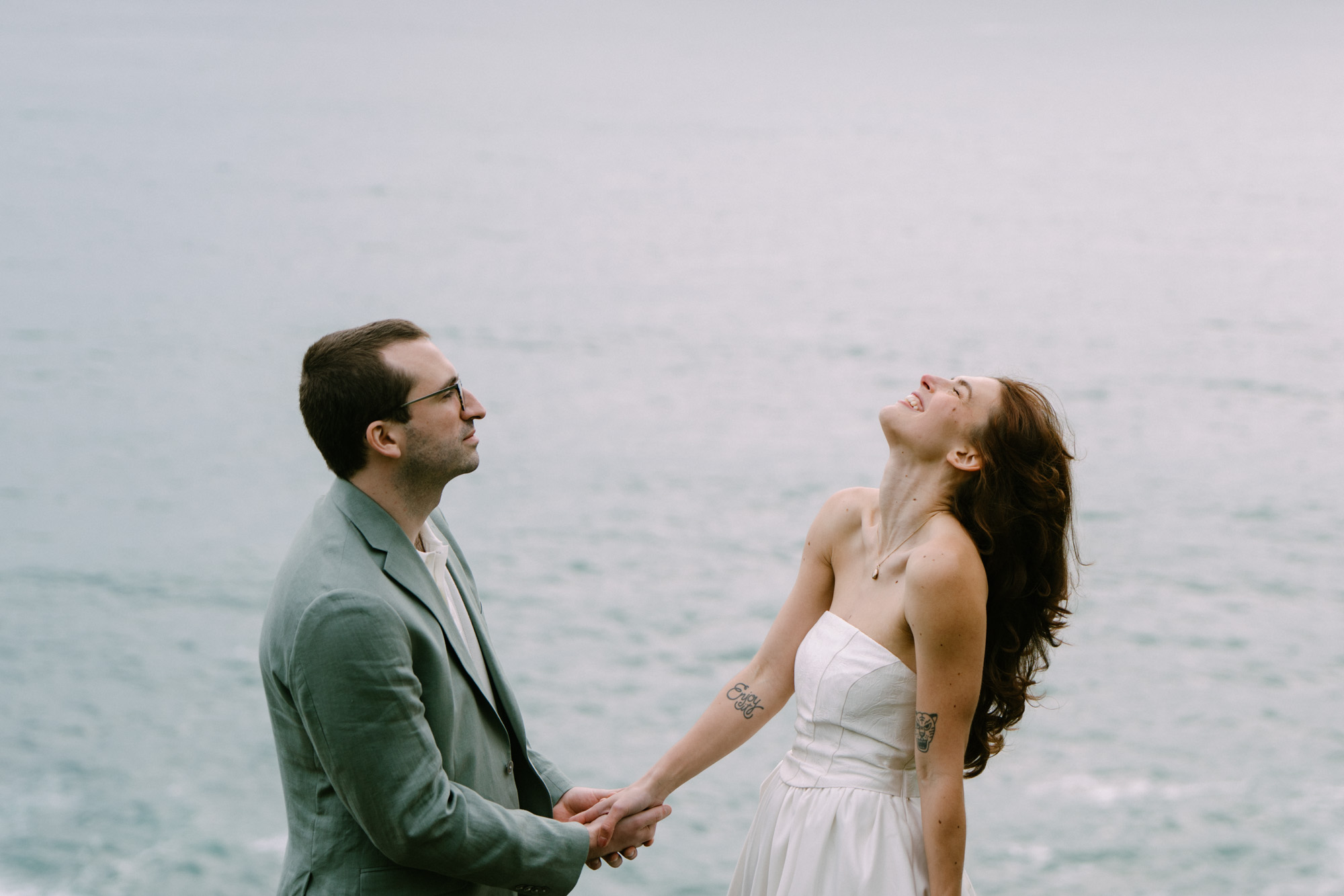 Couple slow dancing and laughing together on a grassy Oregon Coast cliff at Elk Flats, faces turned upward in joy