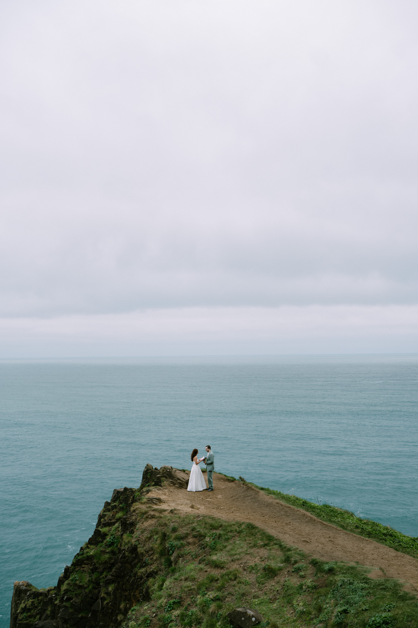 iny figures of a couple on a high coastal bluff at Elk Flats, surrounded by blue-gray ocean on three sides