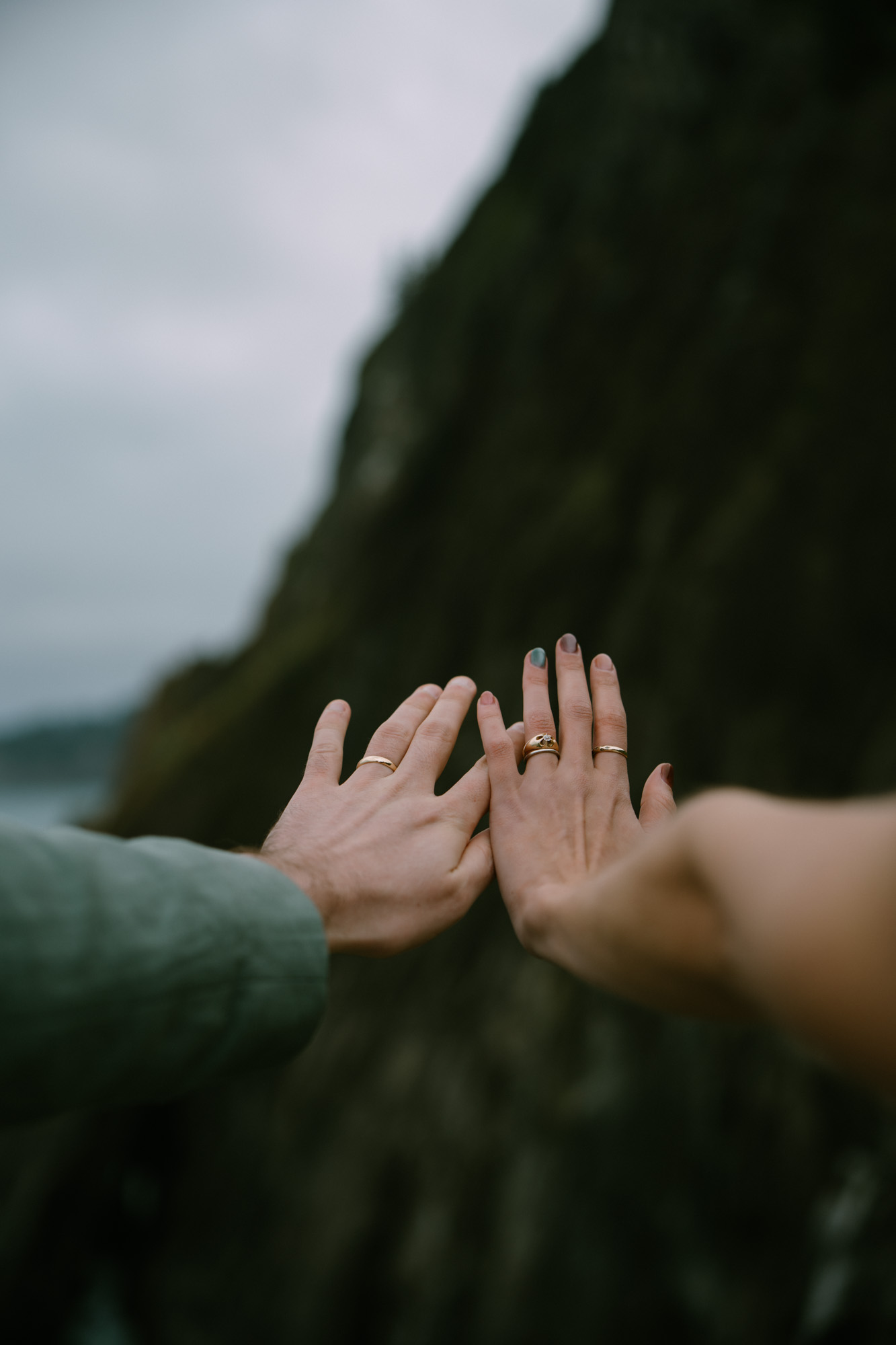 Close-up of two hands reaching toward each other against a blurred Oregon coastal cliff background