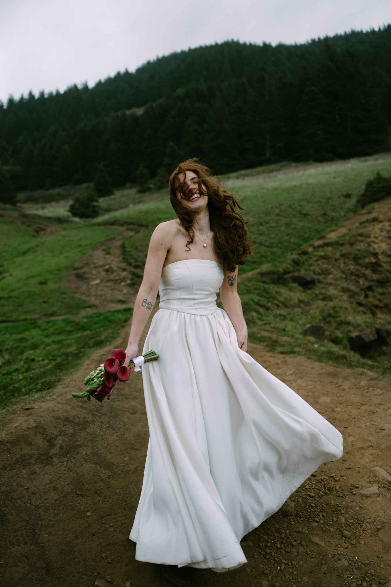 Person in a flowing white strapless dress spinning on a coastal trail at Elk Flats, hair catching the ocean breeze