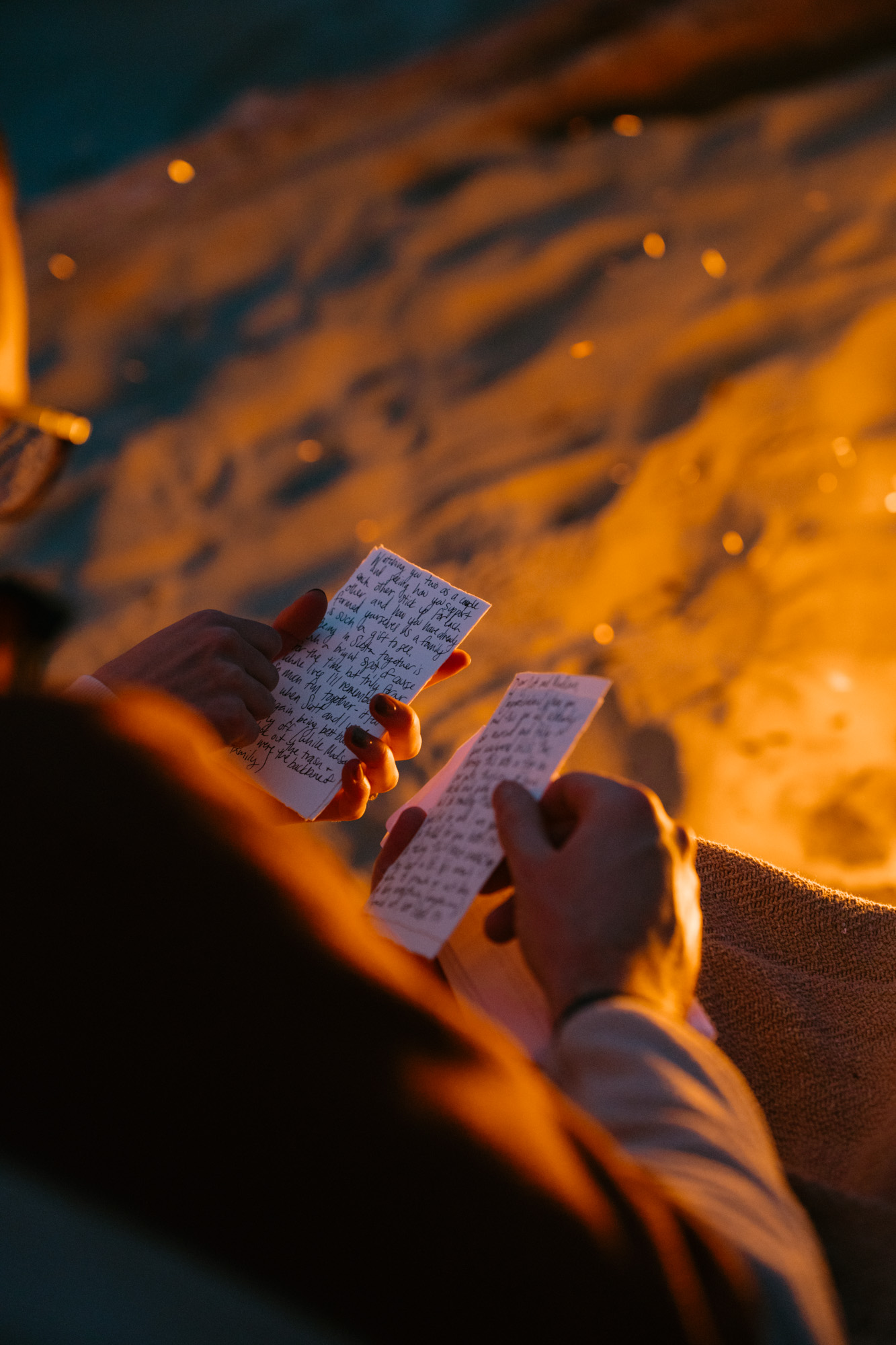 Close-up of hands holding handwritten letters from loved ones by the light of a glowing bonfire at a coastal inn, warm orange firelight