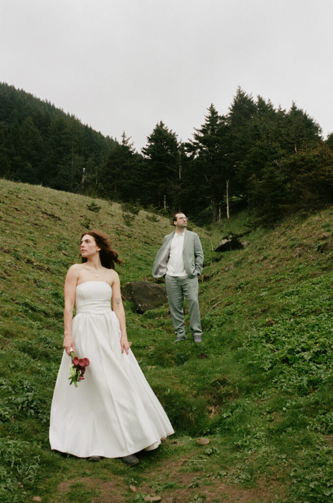 Couple walking through a lush green coastal meadow at Elk Flats, Oregon, white dress contrasting against the wild grass