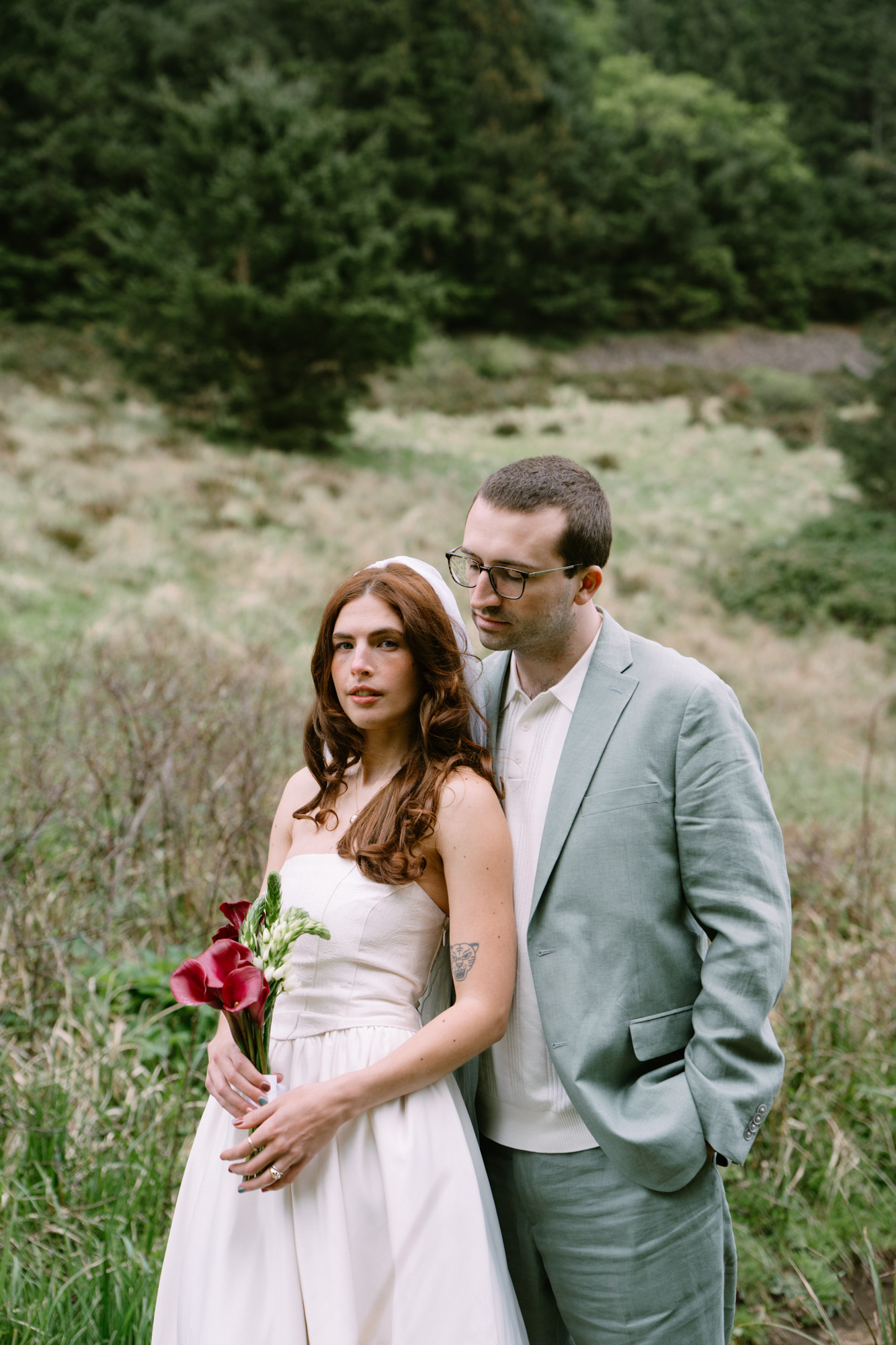 Couple standing together in a windswept coastal meadow at Elk Flats, Oregon, surrounded by wild grasses
