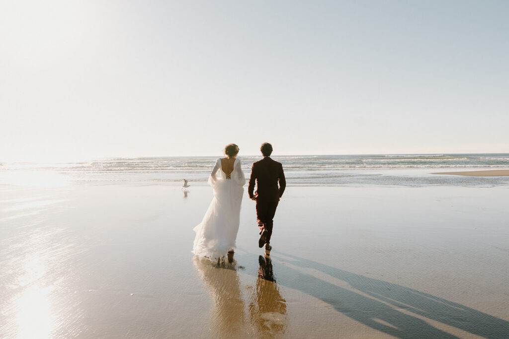 A couple runs towards the ocean on the beach during an Oregon coast elopement. 