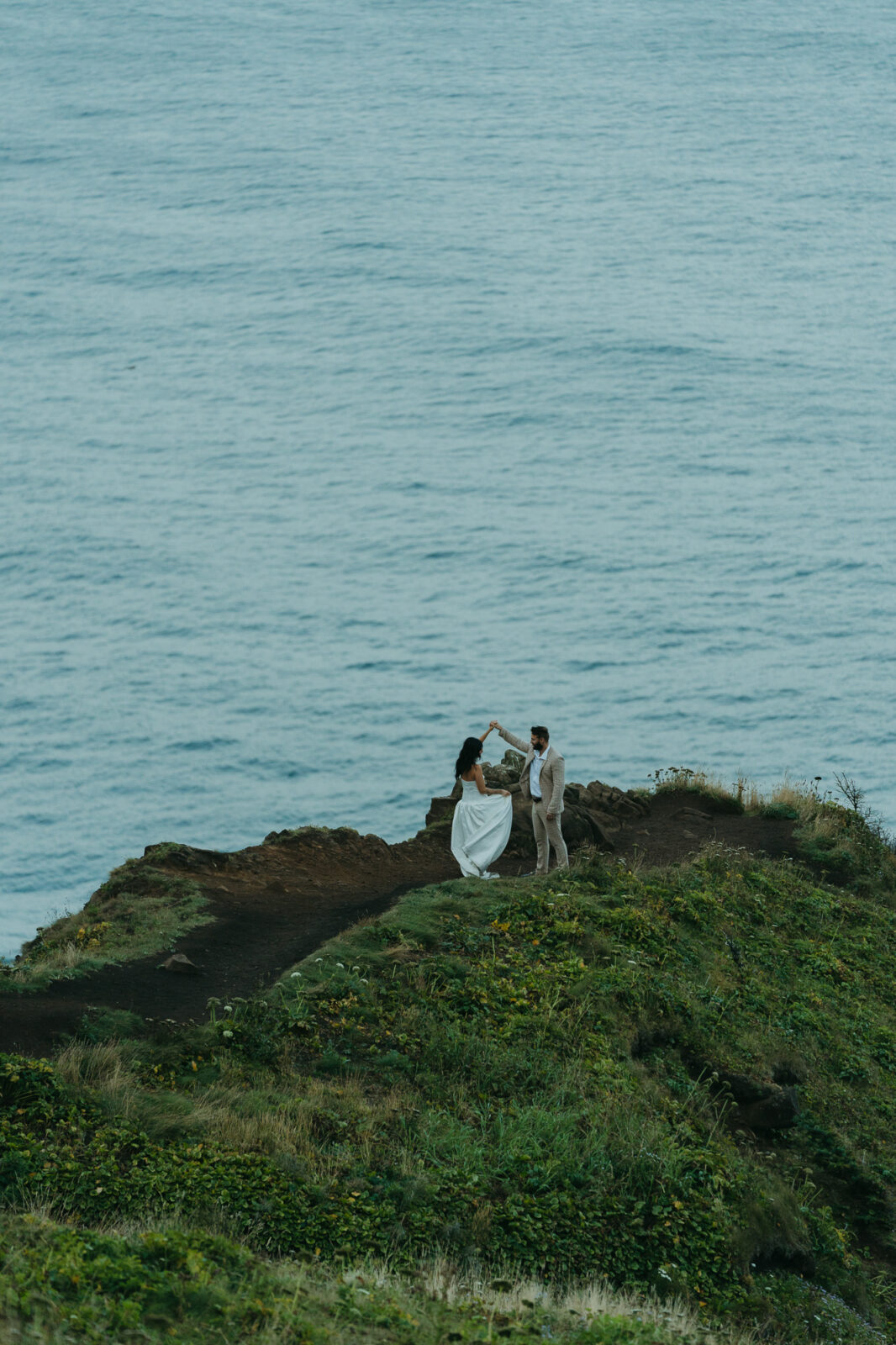 A couple dances on a grassy cliffside overlooking the Pacific Ocean during their Oregon Coast elopement. 