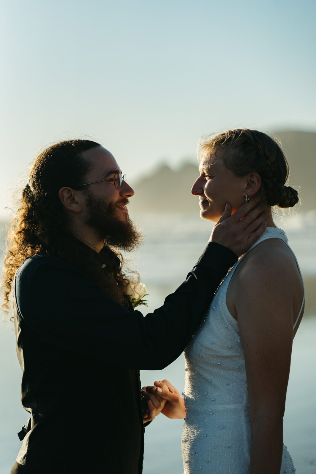 A couple elopes at sunset on the Oregon Coast. There is the ocean, big rocks, and a sandy beach. 