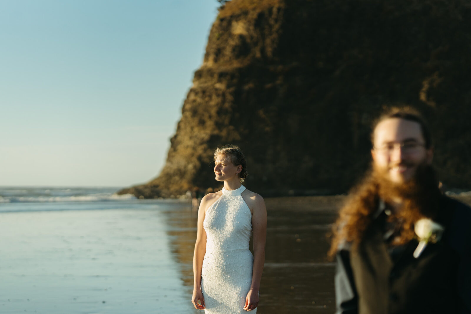 A couple elopes at sunset on the Oregon Coast. There is the ocean, big rocks, and a sandy beach. 