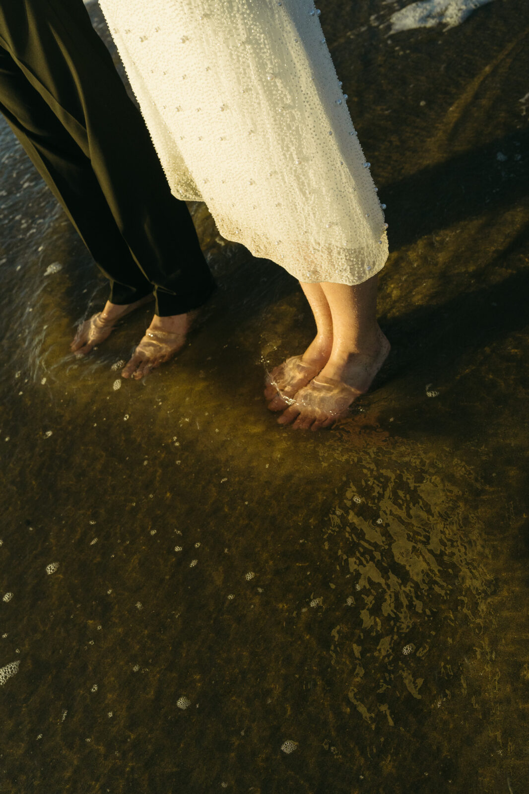 A couple elopes at sunset on the Oregon Coast. There is the ocean, big rocks, and a sandy beach. 