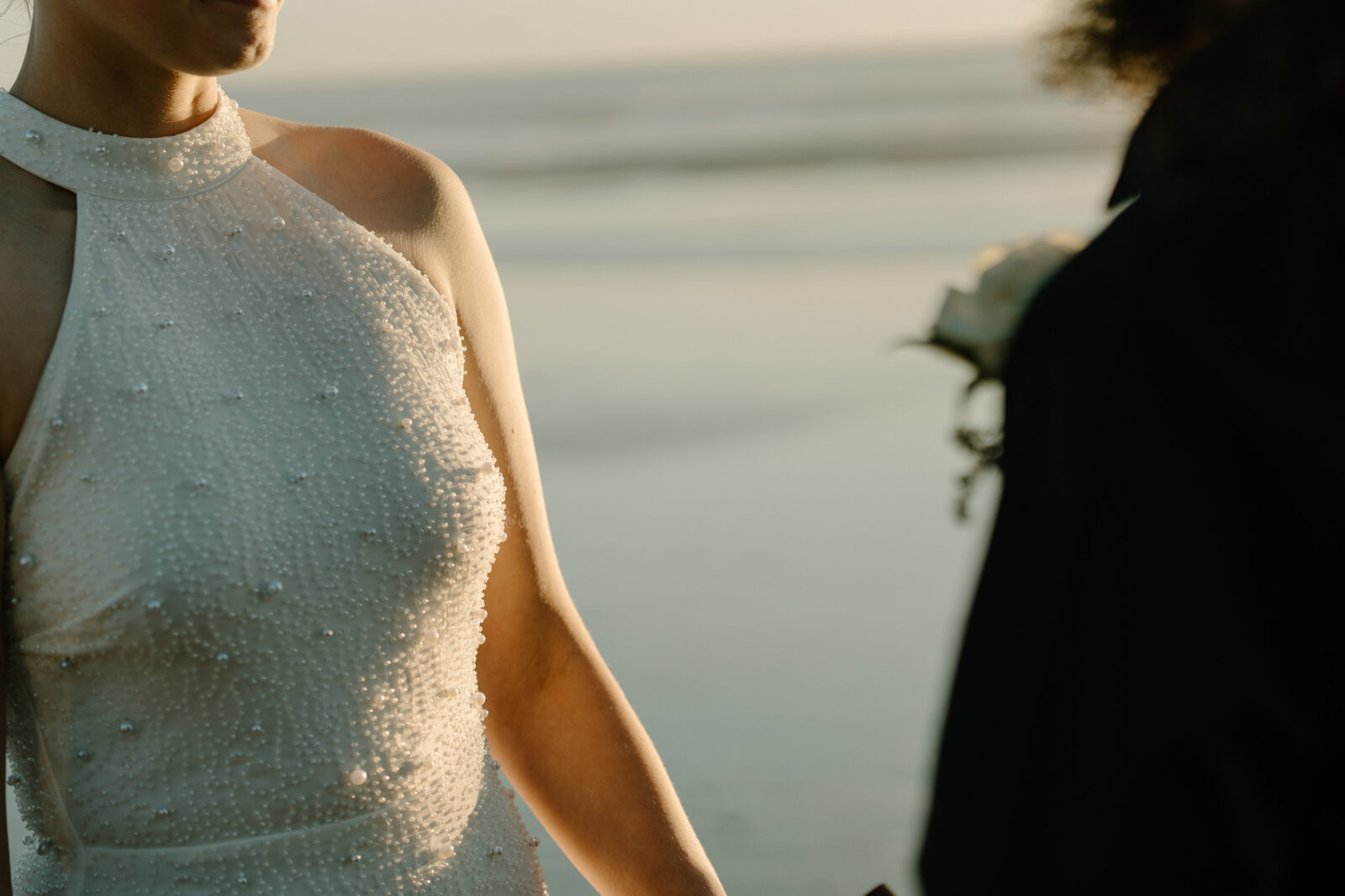 A couple elopes at sunset on the Oregon Coast. There is the ocean, big rocks, and a sandy beach. 