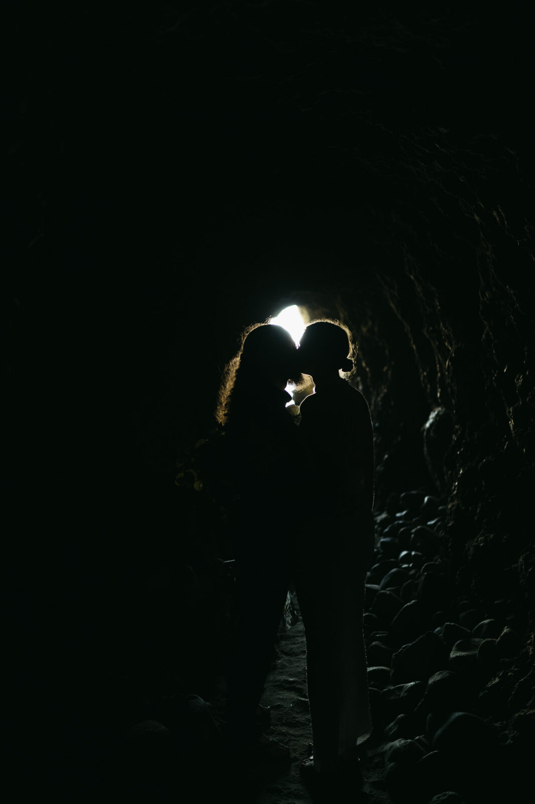 A couple elopes at sunset on the Oregon Coast. There is the ocean, big rocks, and a sandy beach. 