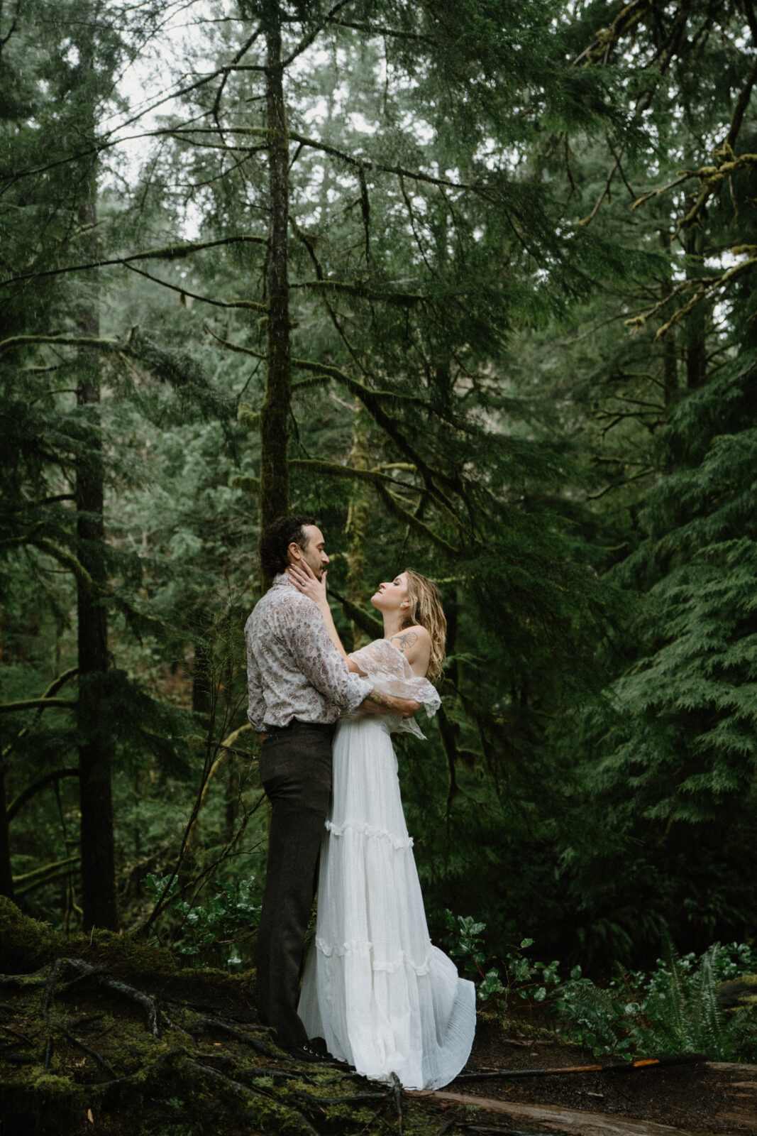 A couple stands on a log in a dark forest and faces each other during their Cannon Beach engagement photo session