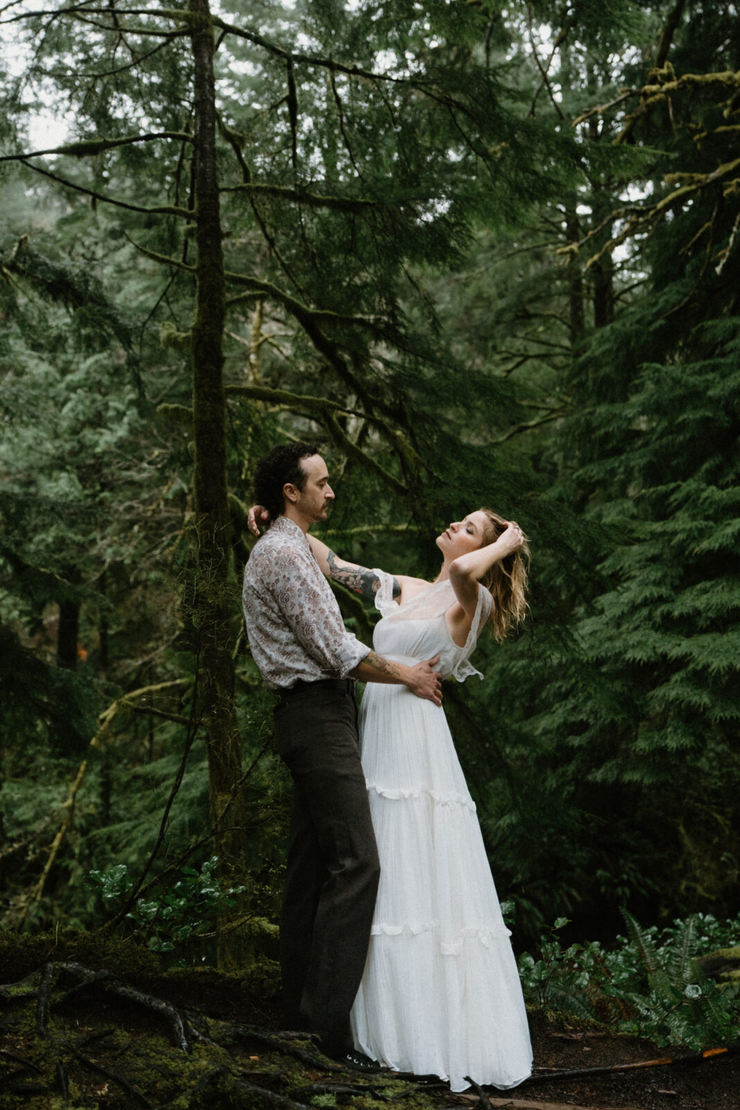 A couple stands on a log in a dark forest and faces each other during their Cannon Beach engagement photo session