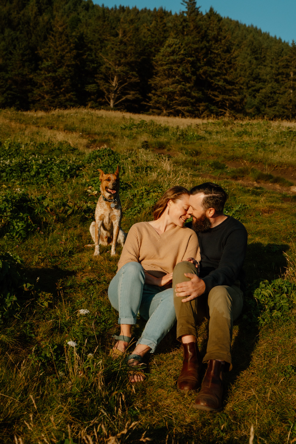 A couple snuggles next to each other with their dog behind them during their Cannon Beach engagement photo session. 