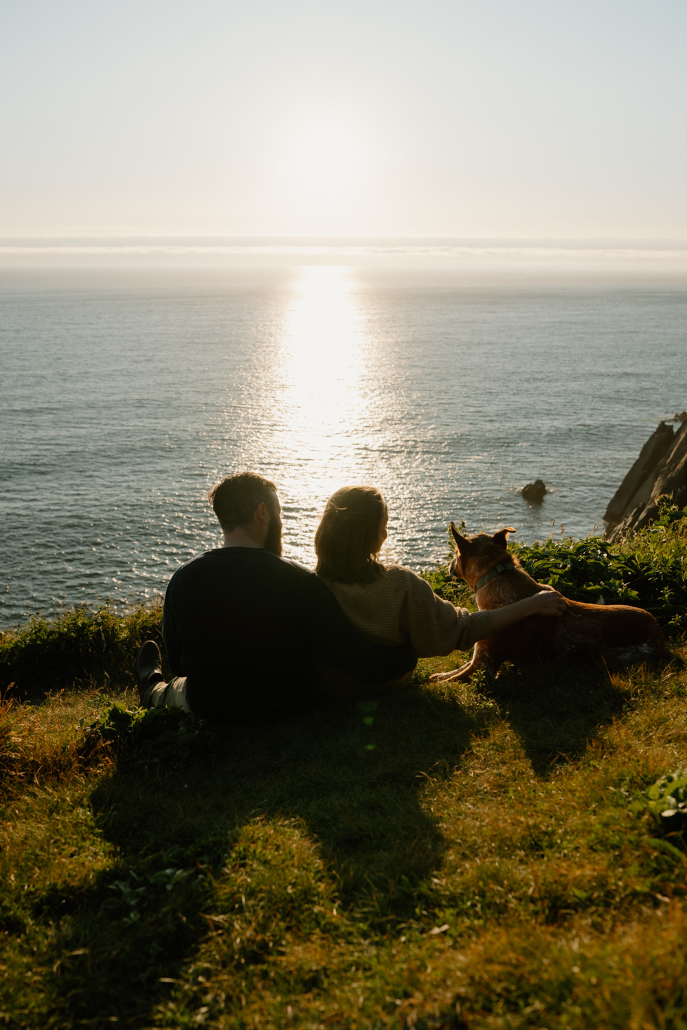 A couple snuggles next to each other with their dog behind them during their Cannon Beach engagement photo session. 