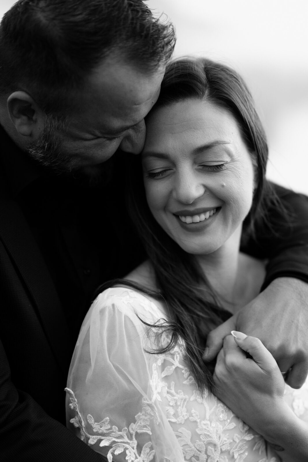 A couple in wedding attire embraces in front of cloud-obstructed mountains during their Lago di Braies elopement. 