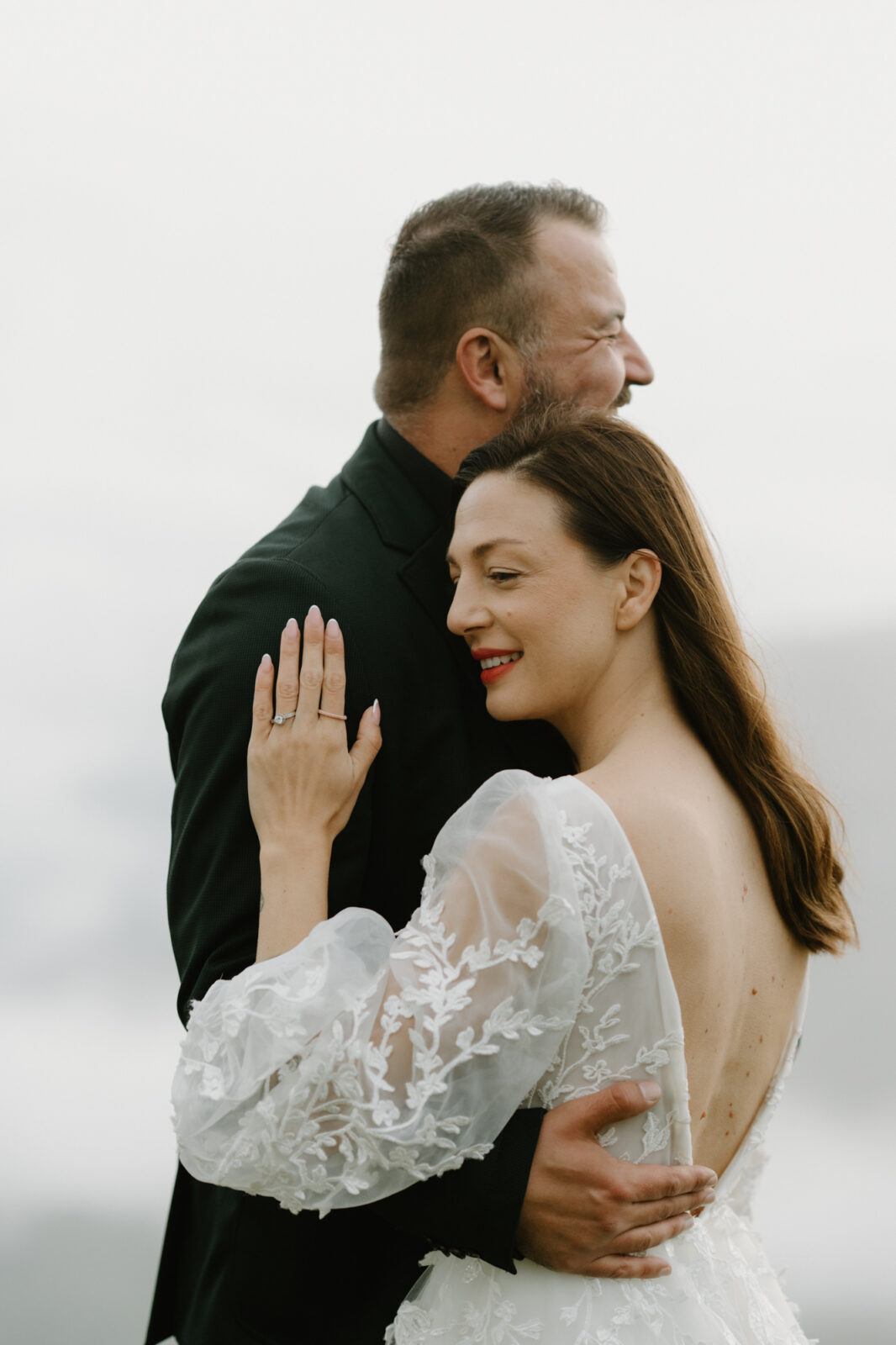 A couple in wedding attire embraces in front of cloud-obstructed mountains during their Lago di Braies elopement. 