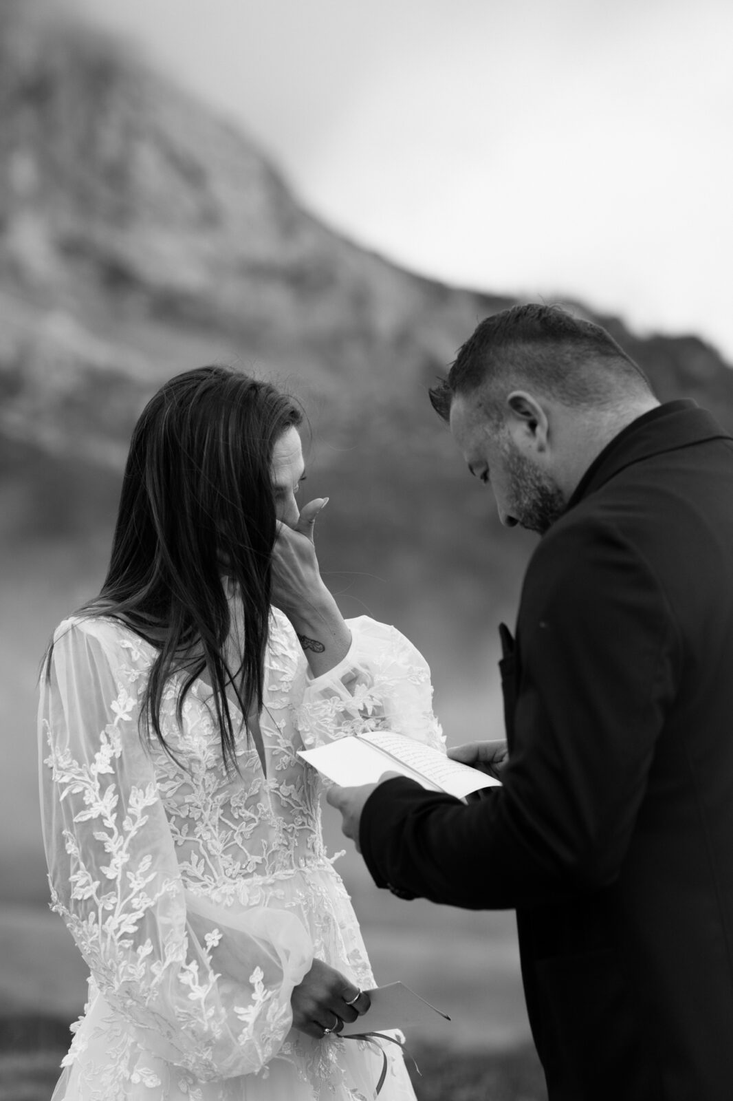 A black and white photo of an emotional couple exchanging wedding vows in front of the mountains during their Lago di Braies elopement. 