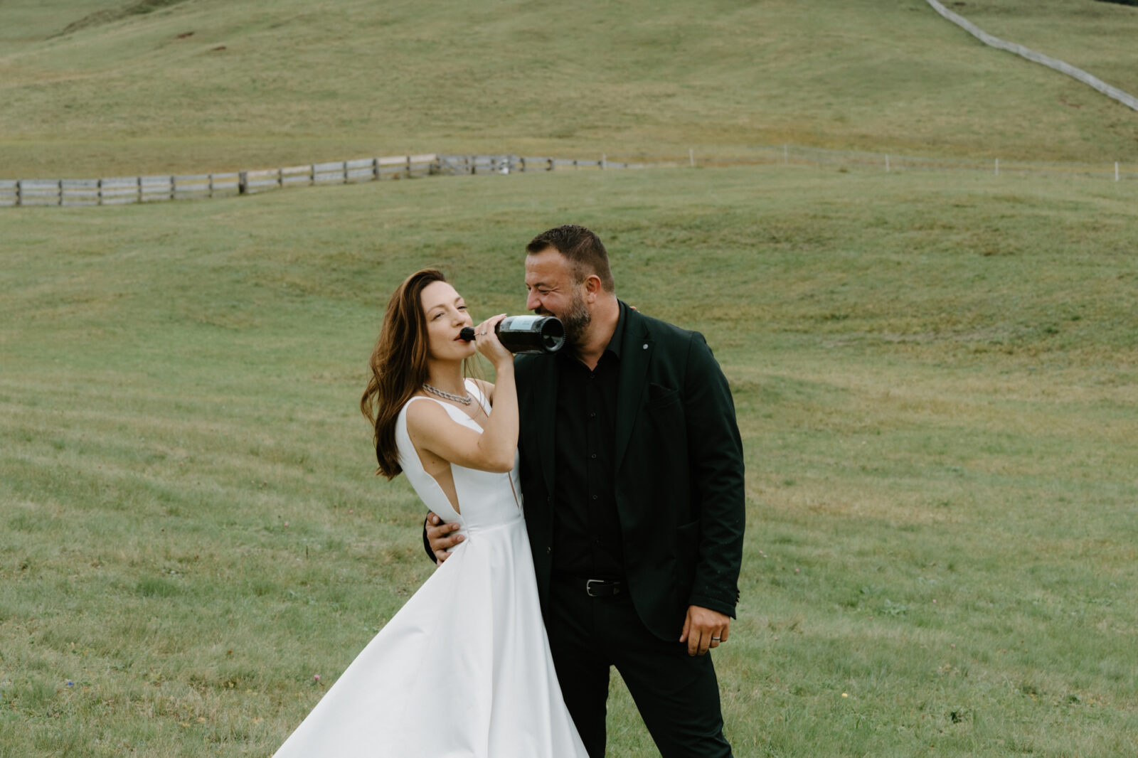 A couple snuggles together while the bride drinks champagne out of the bottle to celebrate their Lago di Braies elopement. 