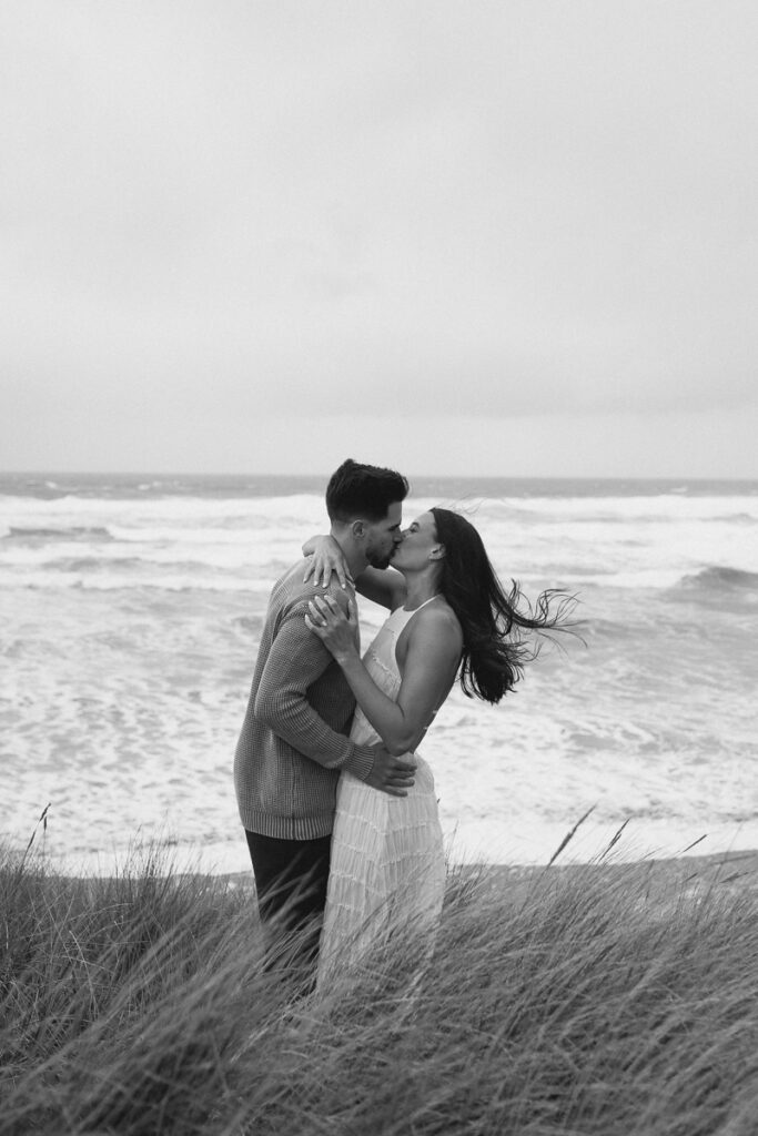 A couple kisses on a cliffside for their Oregon Coast engagement photos.