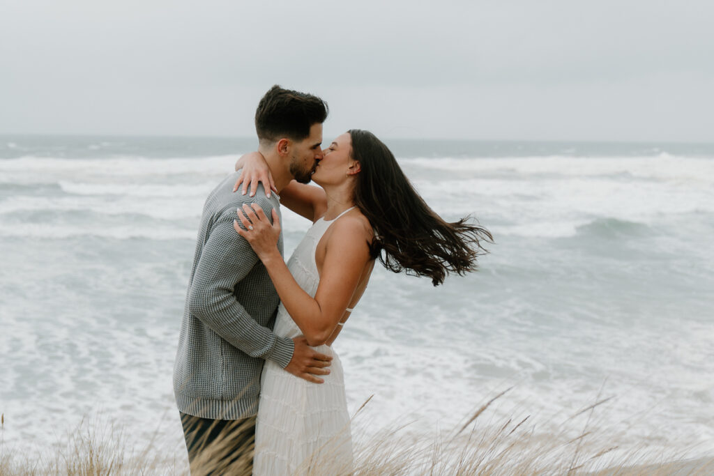 A couple kisses on a cliffside for their Oregon Coast engagement photos.