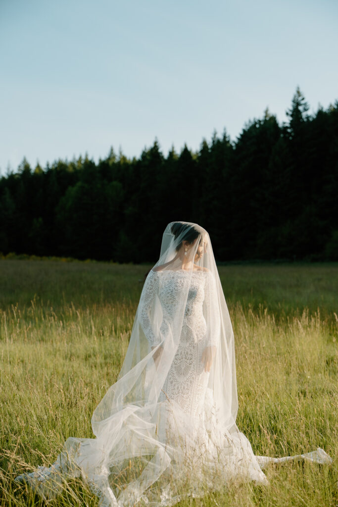 A bride stands in the sun in a field during her Wind Mountain Ranch wedding. 