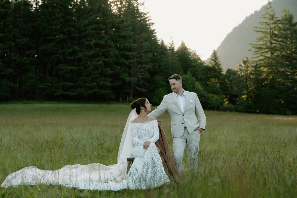 A couple sits in a field next to each other at sunrise before their wedding at Wind Mountain Ranch.