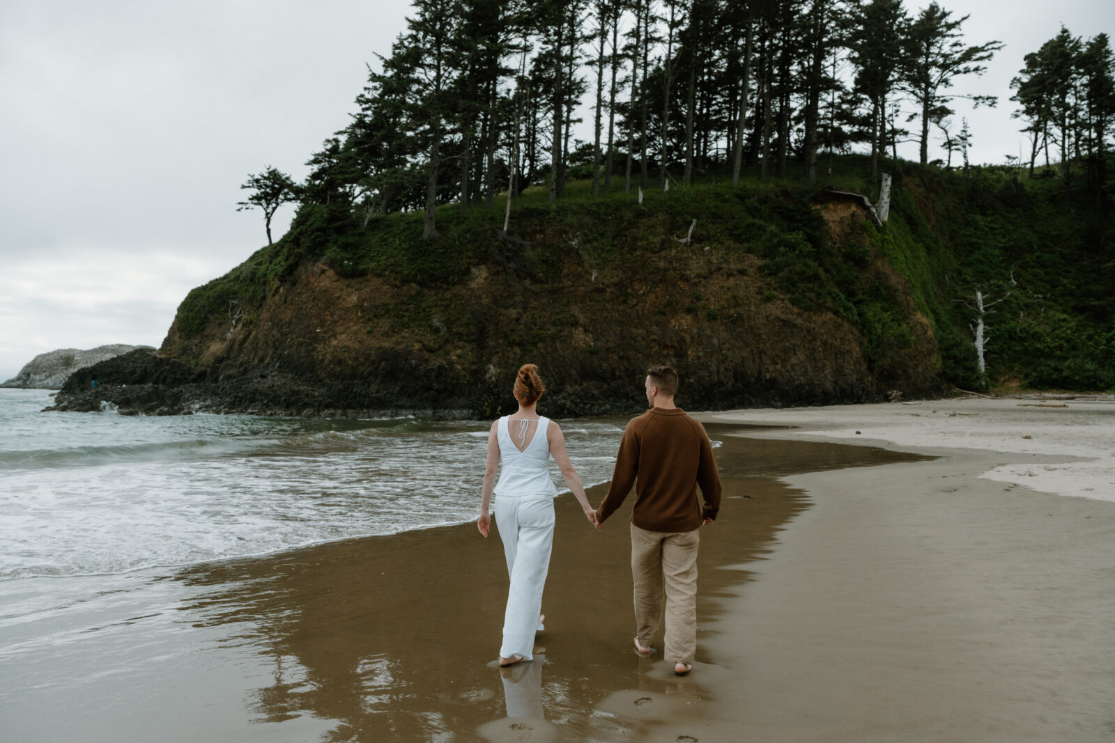 A man and woman walk together and laughs as they splash in the ocean after their Oregon Coast proposal.