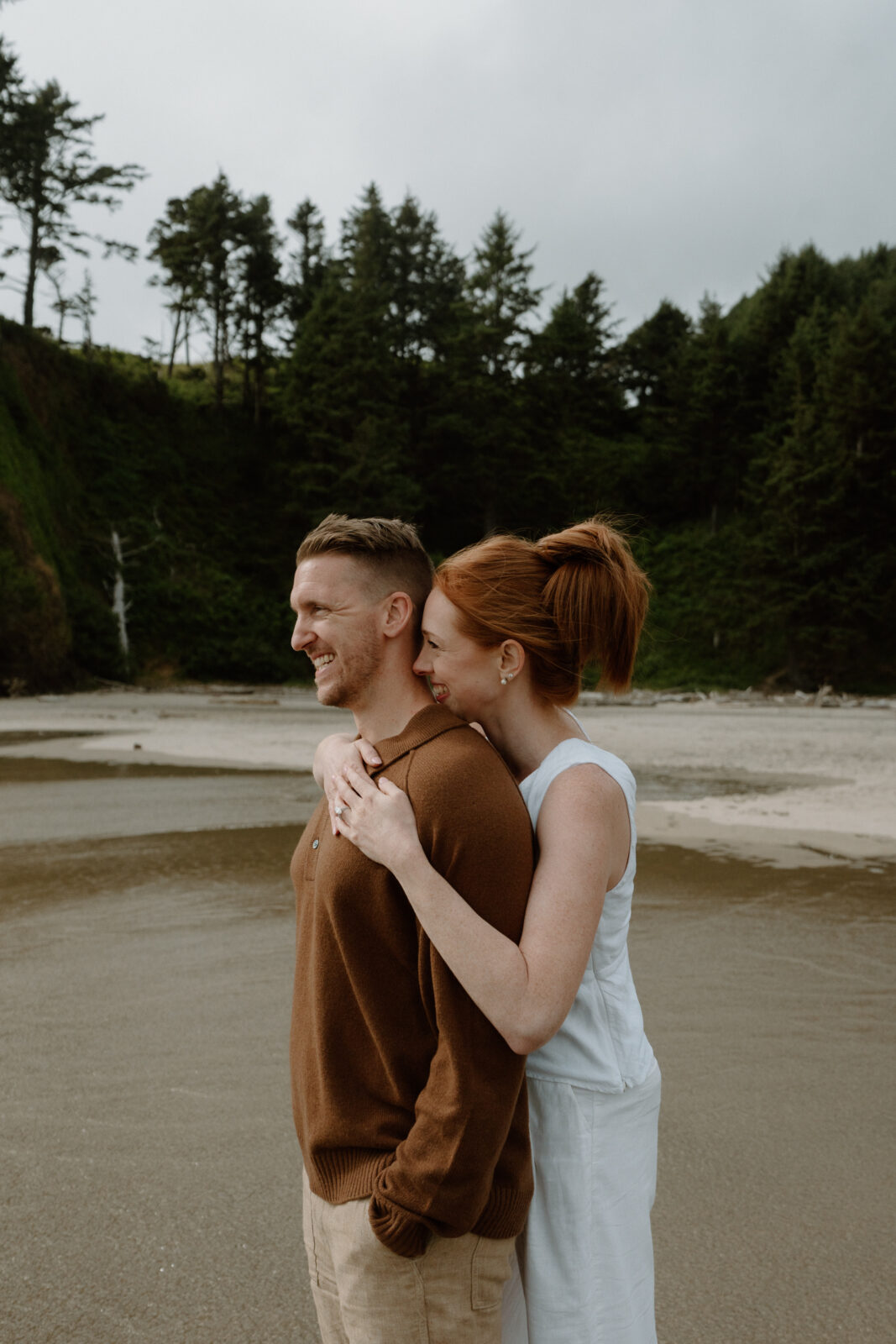 A couple stands in the water and looks out at the ocean after their Oregon Coast proposal.