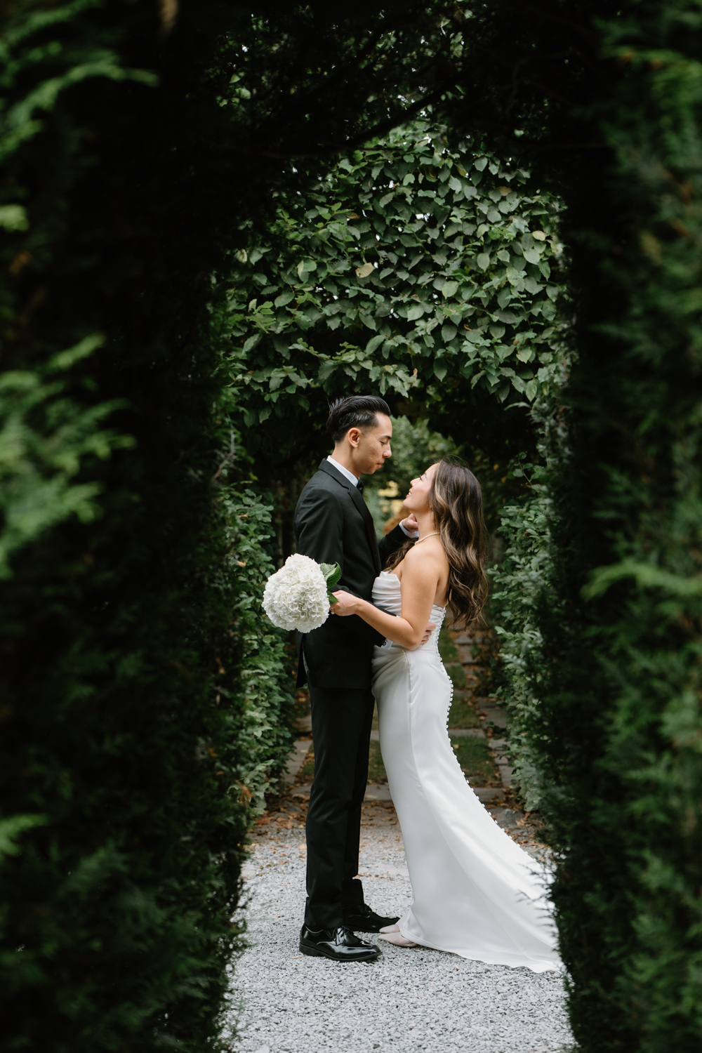 A couple in wedding attire snuggles together in a garden at their Briarwood Estate wedding.