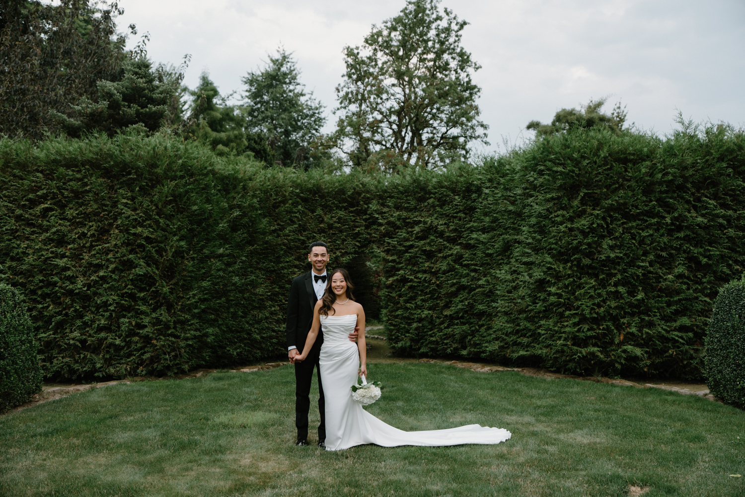A couple in wedding attire snuggles together in a garden at their Briarwood Estate wedding.