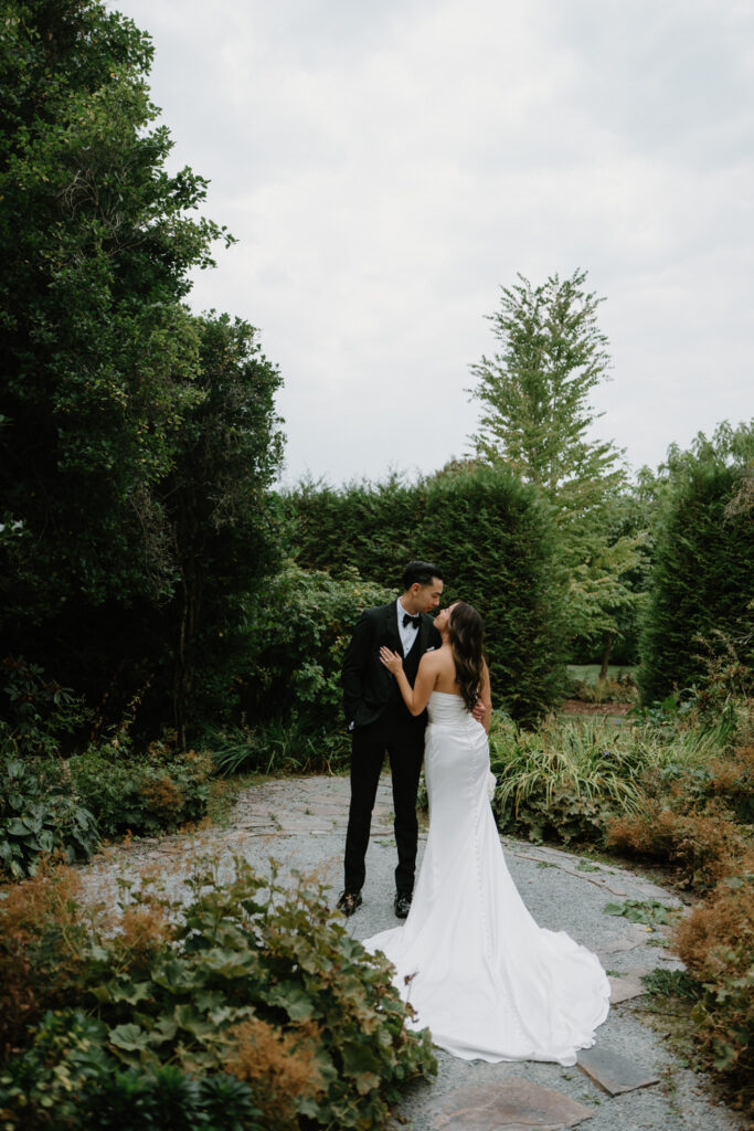 A couple in wedding attire snuggles together in a garden at their Briarwood Estate wedding.