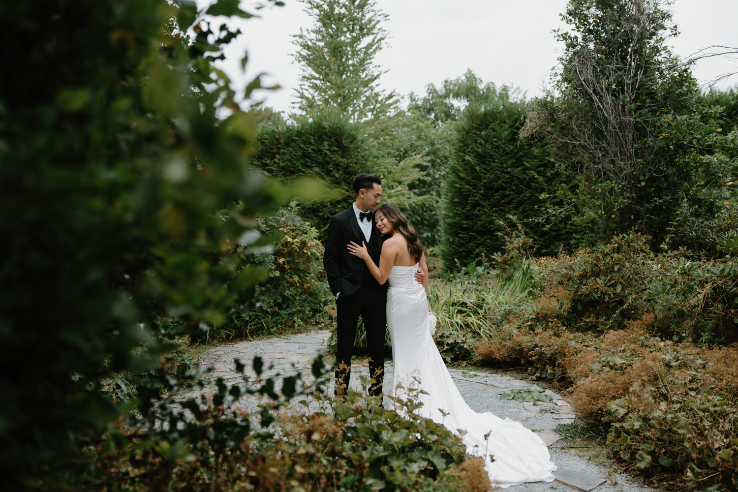 A couple in wedding attire snuggles together in a garden at their Briarwood Estate wedding.