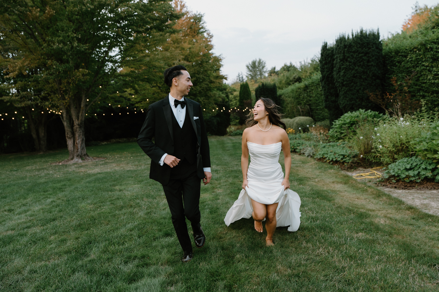 A couple in wedding attire runs through a field at sunset during their Briarwood Estate wedding.