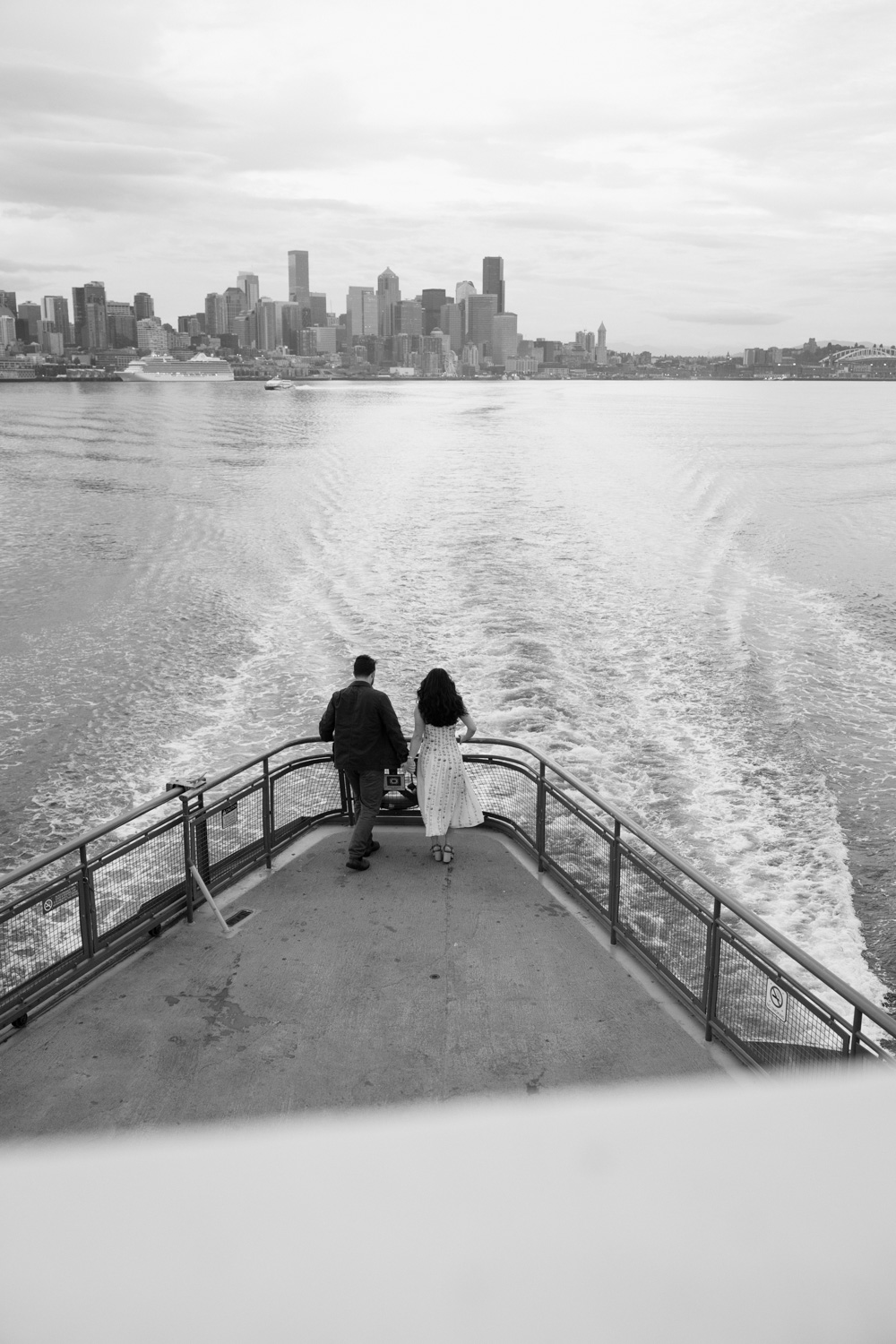 A couple looks over the ledge of a ferry for their Seattle ferry engagement photos.