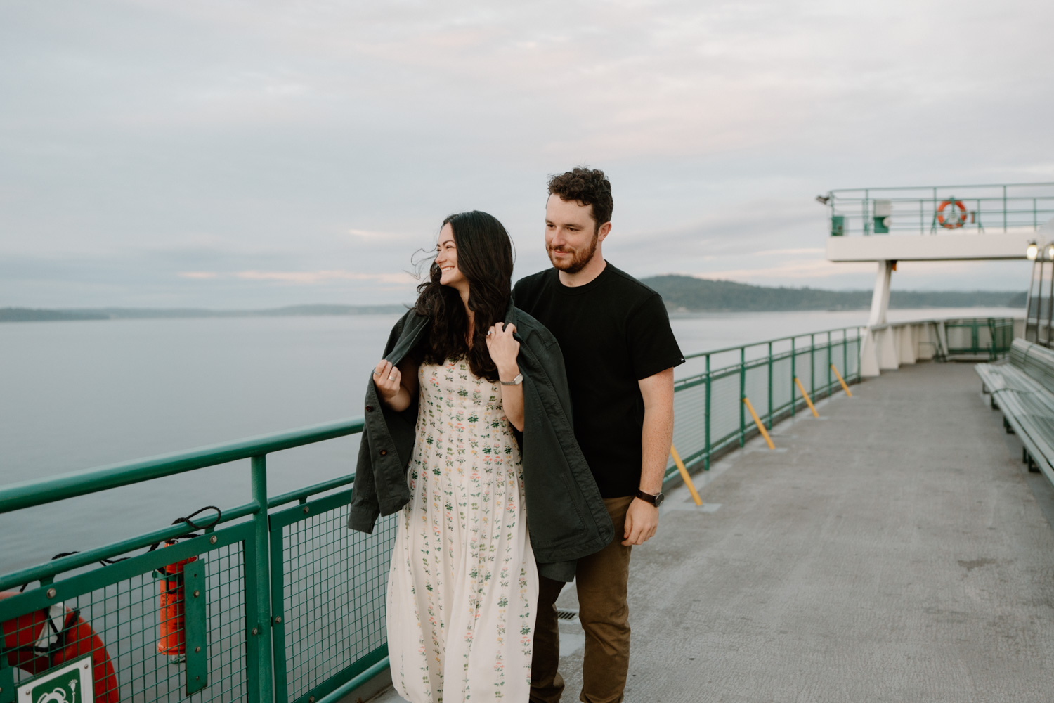 A couple cozies up and looks out at the water during their Seattle ferry engagement photo session.