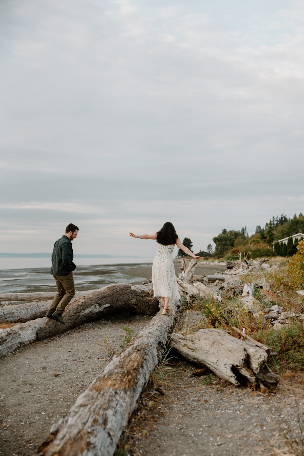 A couple holds hands on a rocky beach on bainbridge island during their seattle ferry engagement photos session.