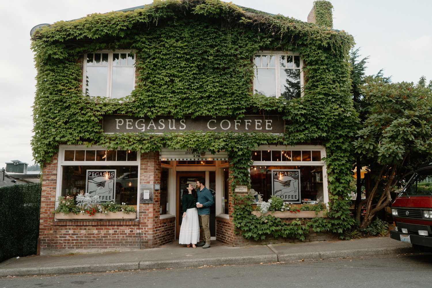 A couple stands outside of an ivy covered coffee shop on Bainbridge island during their seattle ferry engagement photos session.