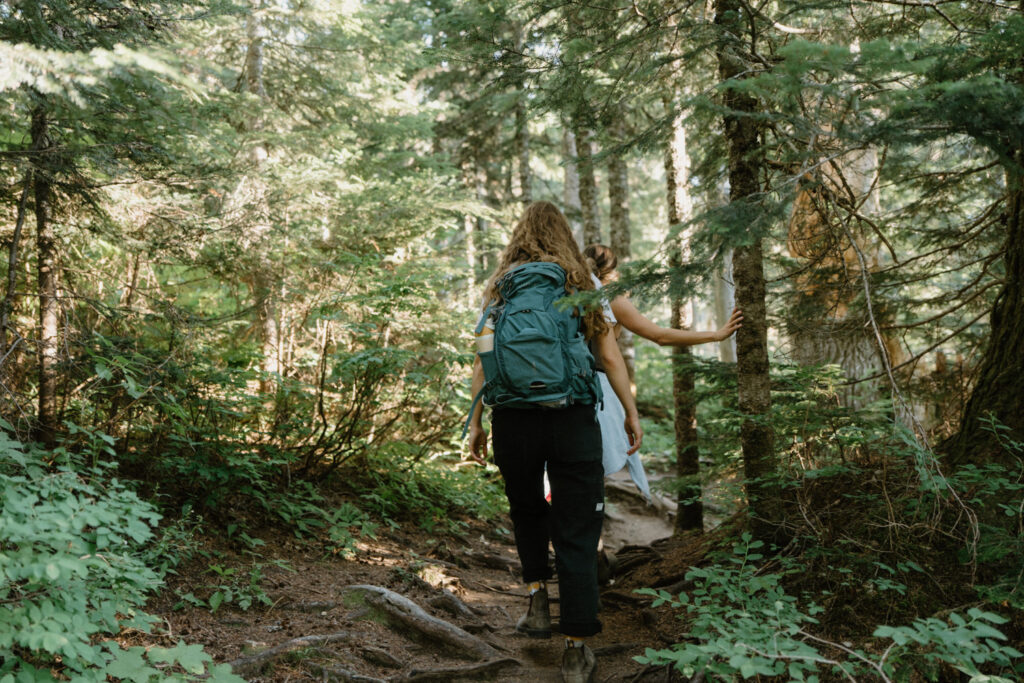 A couple hikes through the woods in hiking attire for their Mount Hood elopement