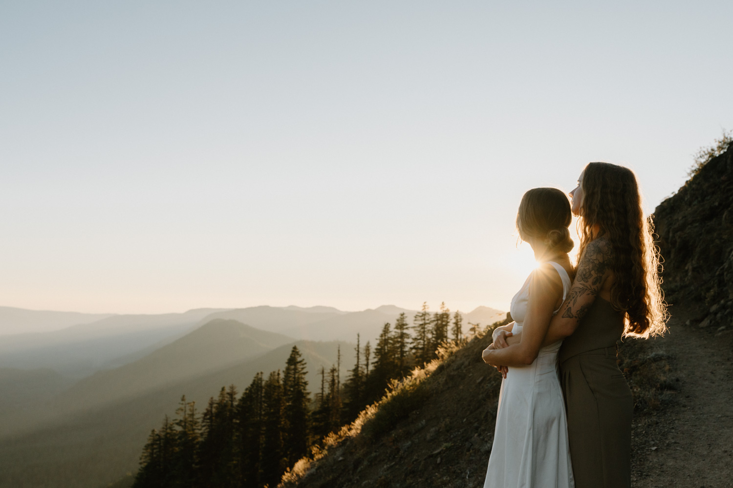 A couple embraces with the sunset and a dark forest behind them during their Mount Hood elopement