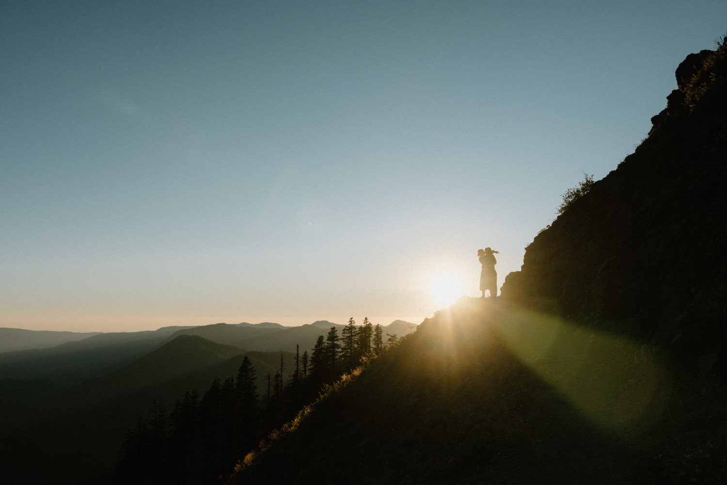 A couple embraces with the sunset and a dark forest behind them during their Mount Hood elopement