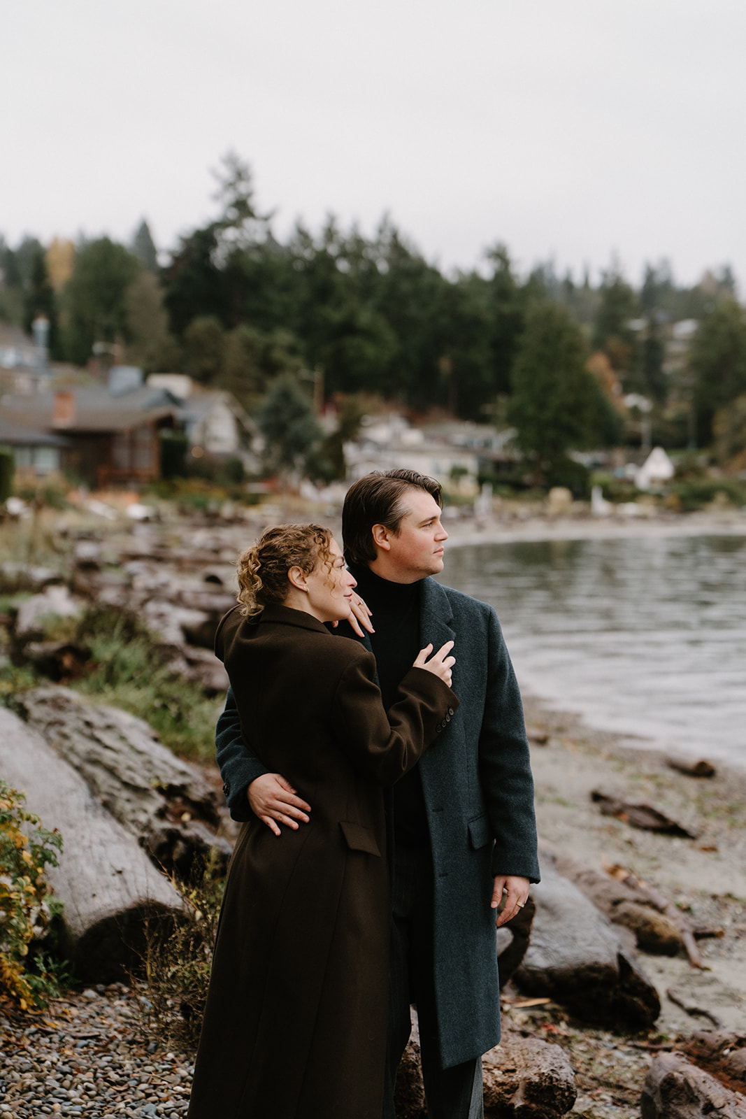 A couple snuggles on a shoreline in the winter Black and white photo of a couple walking in a park for their Seattle engagement photos