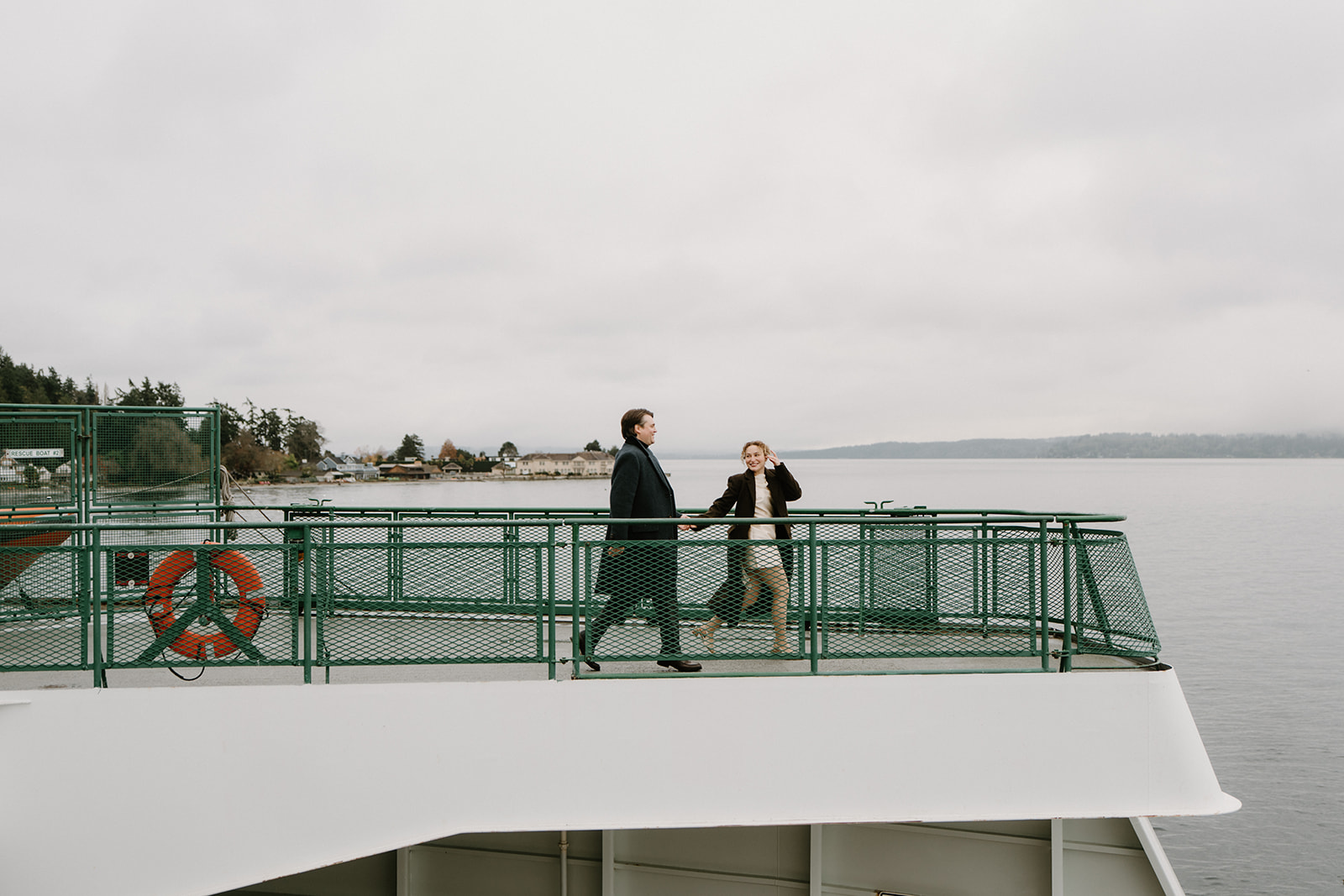 A far away photo of a couple holding hands and running on the Vashon Island ferry for their Seattle engagement photos
