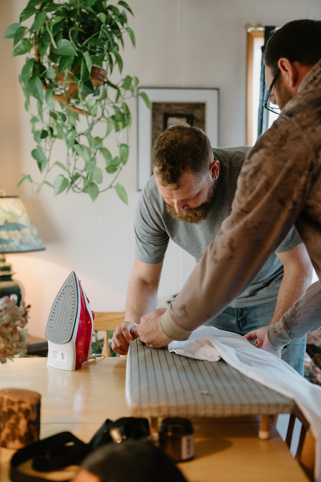 A man and his friend iron a shirt in a beach Airbnb for a Florence, Oregon elopement.