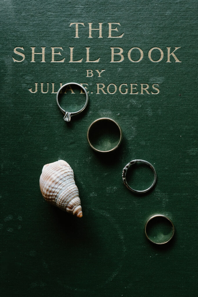 A dark green book with a shell and four wedding rings spread out on it for a Florence, Oregon elopement.